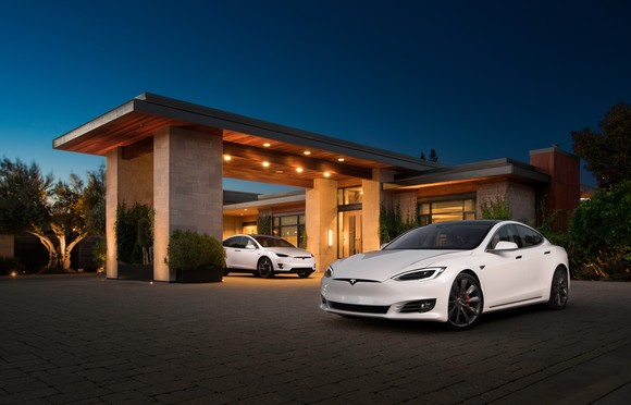 Two white Teslas parked in front of a building at twilight.