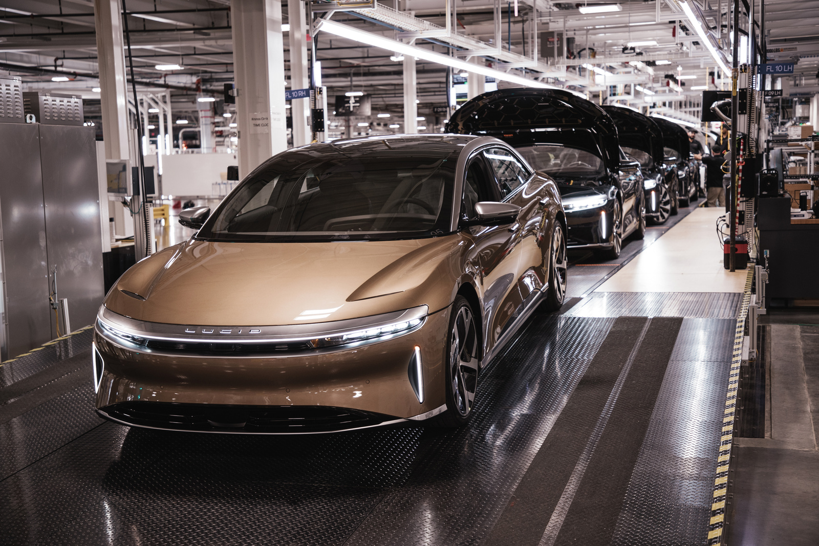 gold Lucid Air EV in front of row of cars on production line. 
