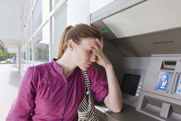 A person in a purple blouse frowns, leaning on an ATM machine.