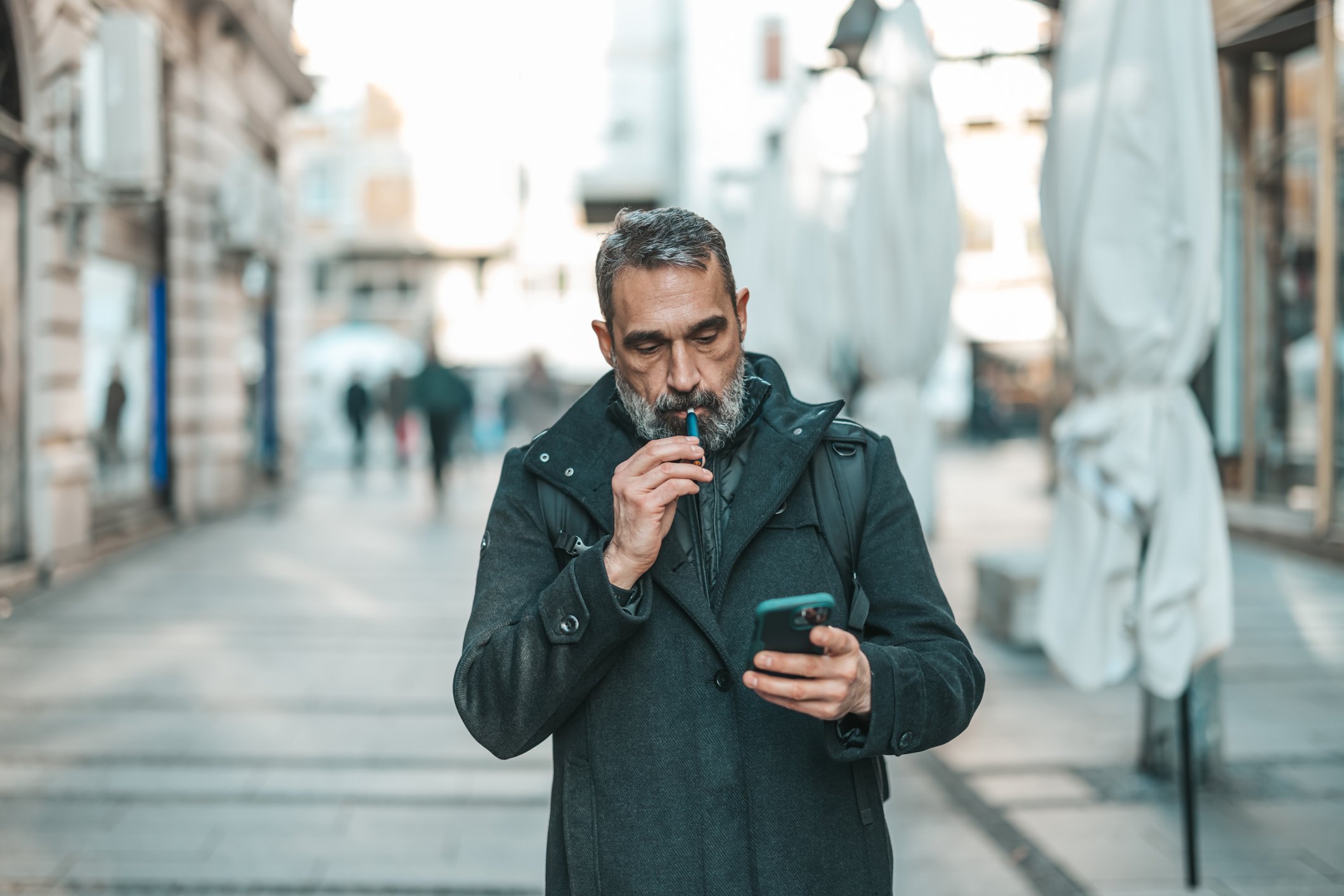 Person walking down the street looking at a phone and vaping.