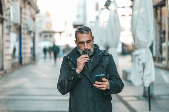Person walking down the street looking at a phone and vaping.