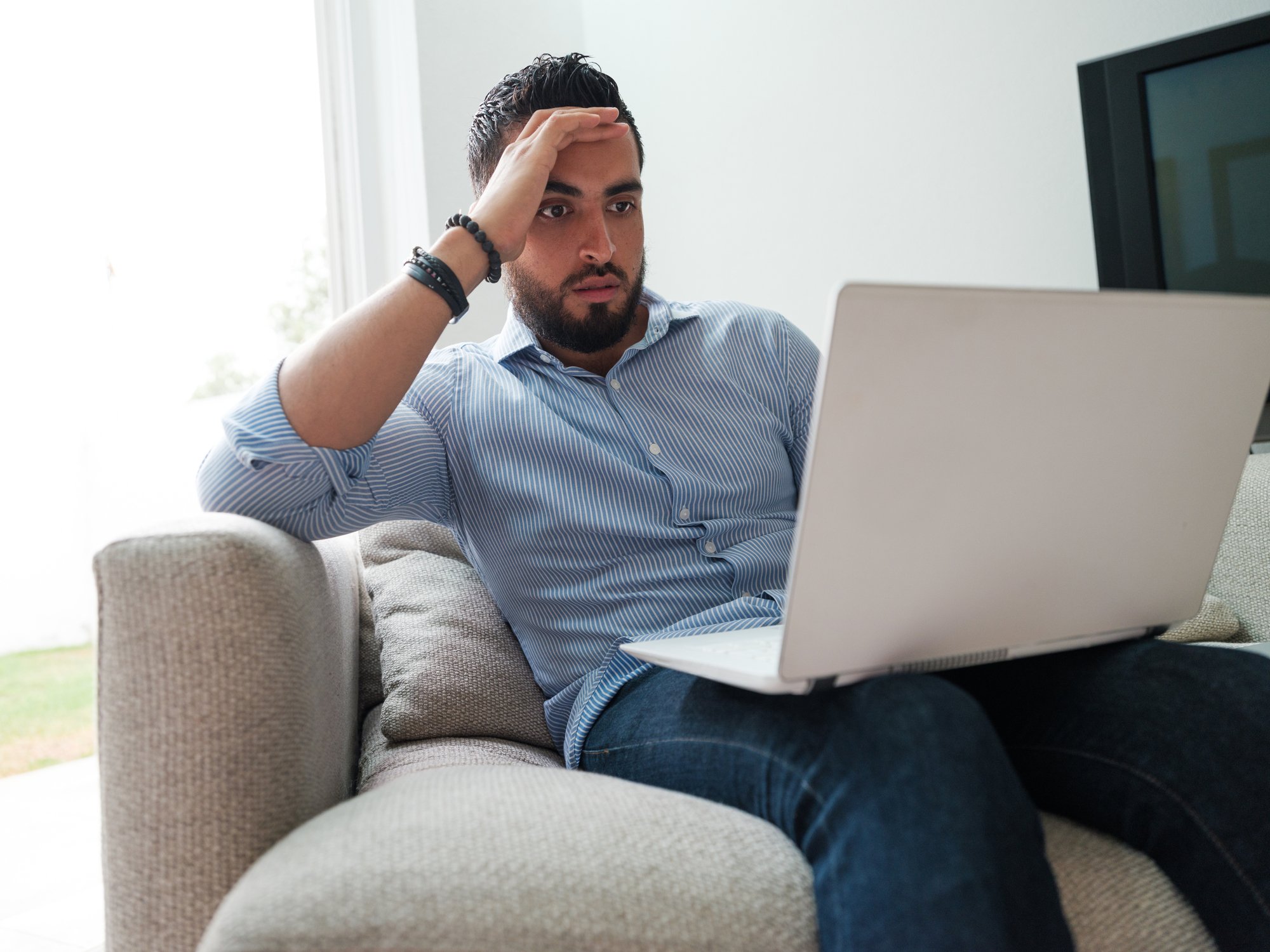 A person with a concerned facial expression looking at a laptop.