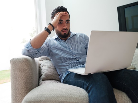 A person with a concerned facial expression looking at a laptop.