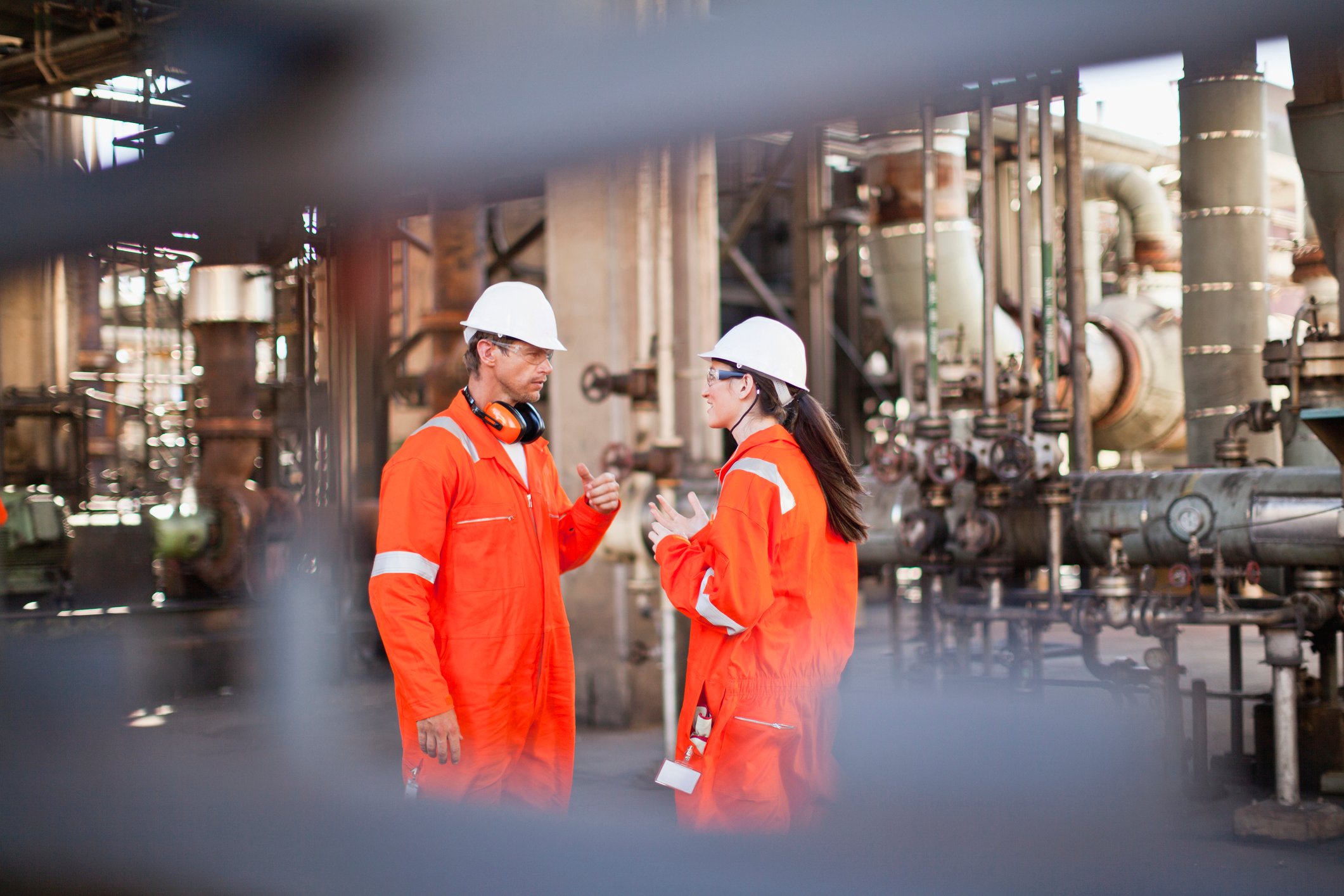 Two workers in orange suits and hard hats at an energy plant.