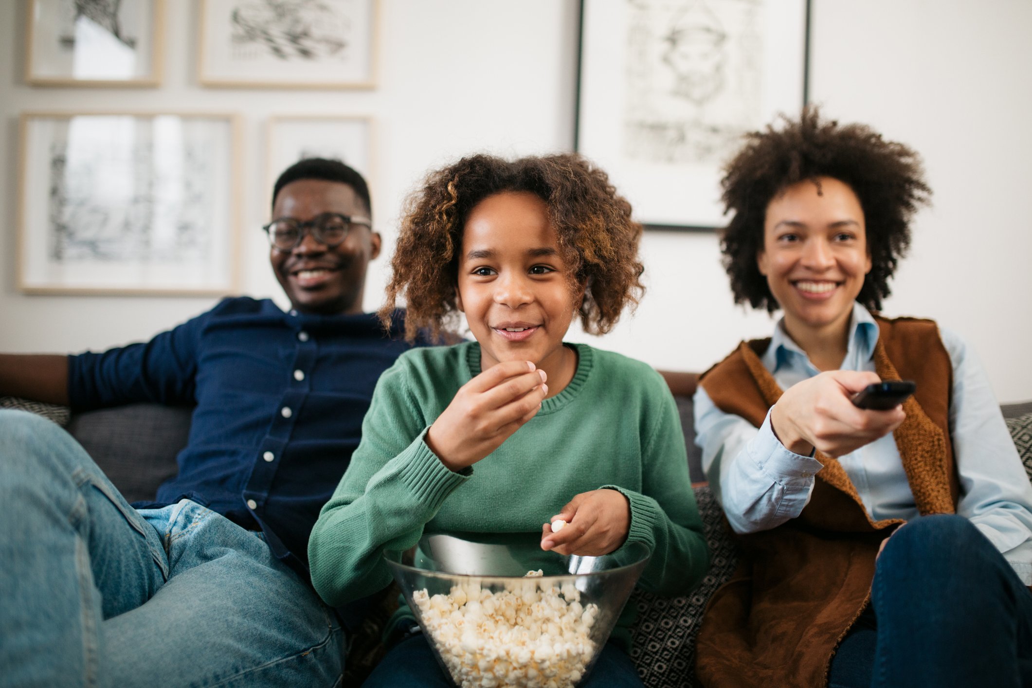 family of three eating popcorn and watching TV from couch.