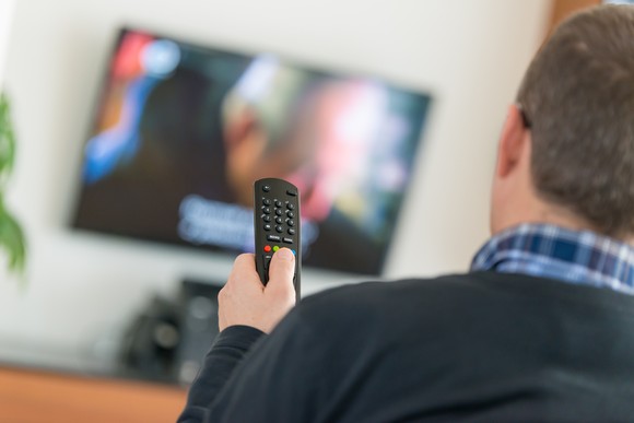 Over-the-shoulder shot of man operating his TV on the wall with remote. 