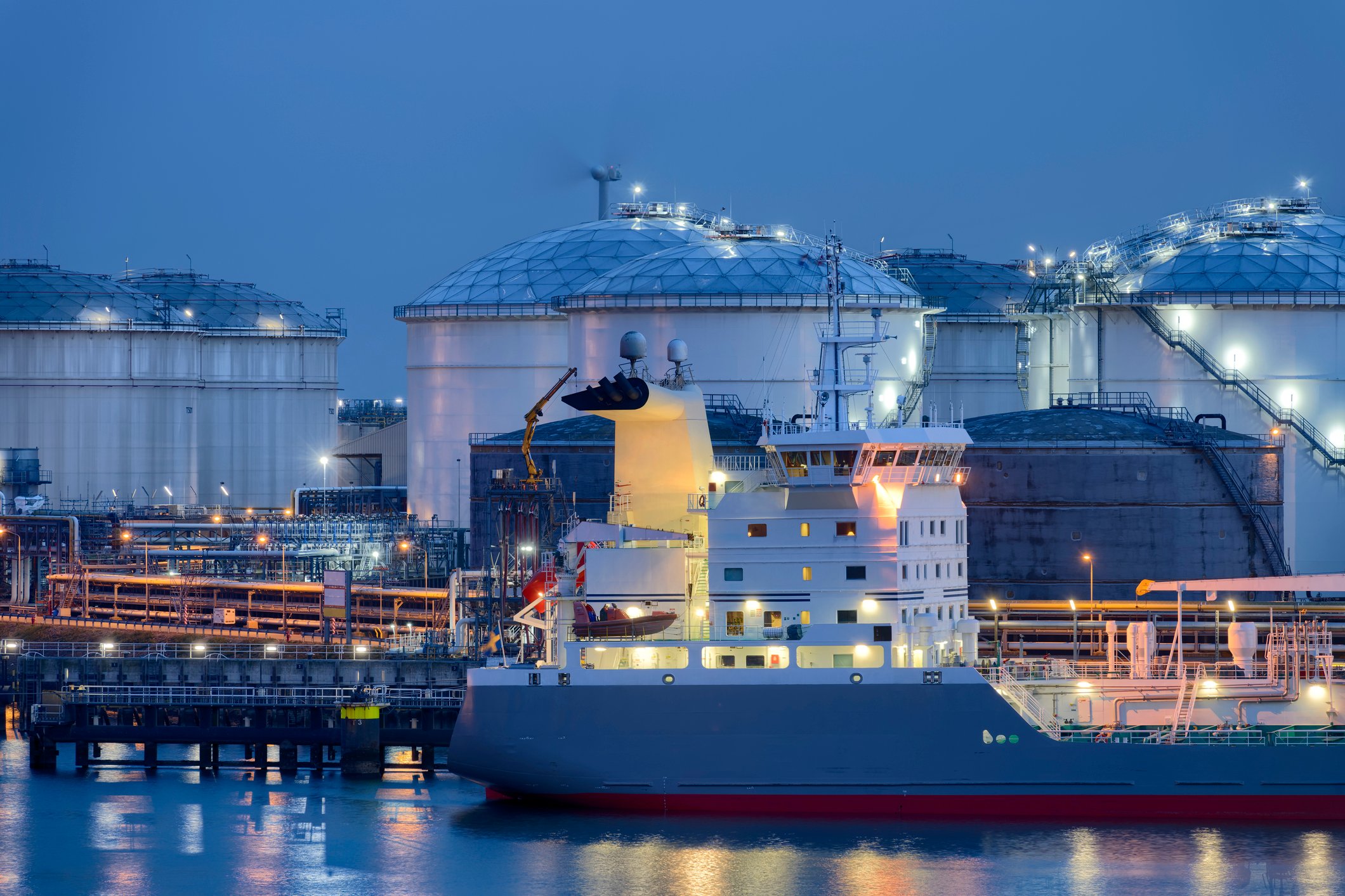 A liquefied natural gas (LNG) terminal with a tanker in front, at either dusk or dawn.