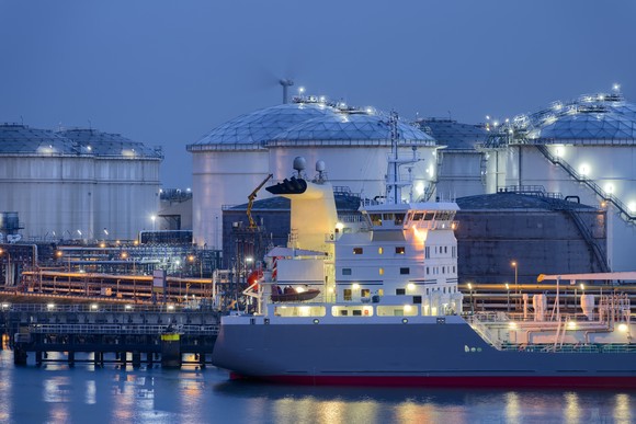 A liquefied natural gas (LNG) terminal with a tanker in front, at either dusk or dawn.