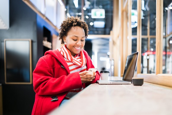 A person sitting at a laptop, smiling while using their phone.