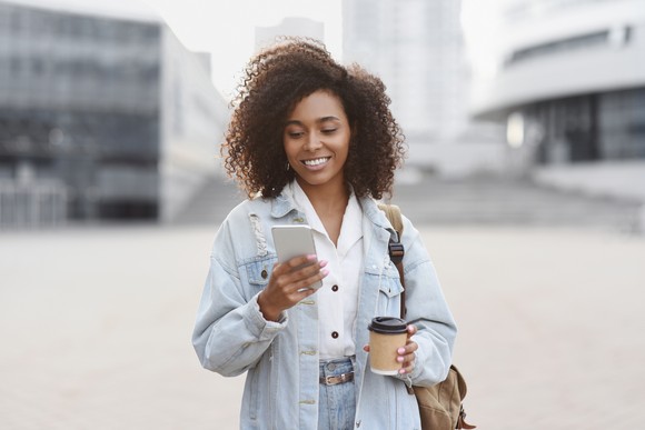 A person checks a smartphone while drinking a coffee.