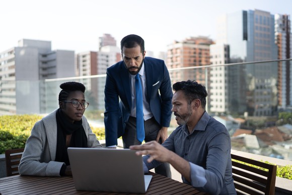 Three people looking at laptop in outdoor office area.