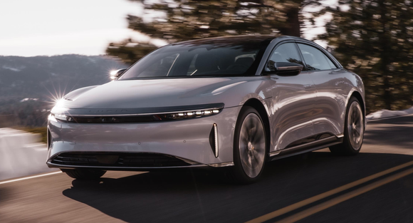 Silver Lucid Air sedan driving on scenic roadway.