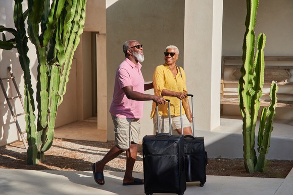 Two mature people walk with their rolling suitcases.