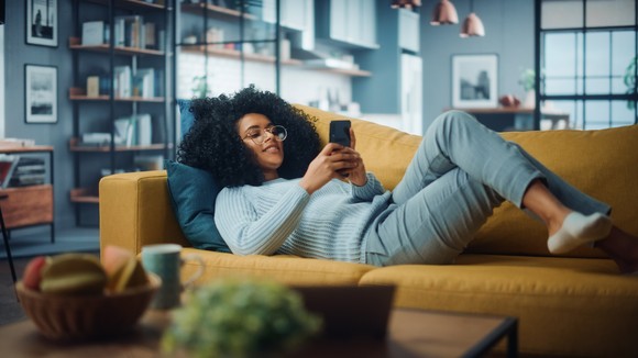 Person laying on couch and shopping on their phone.
