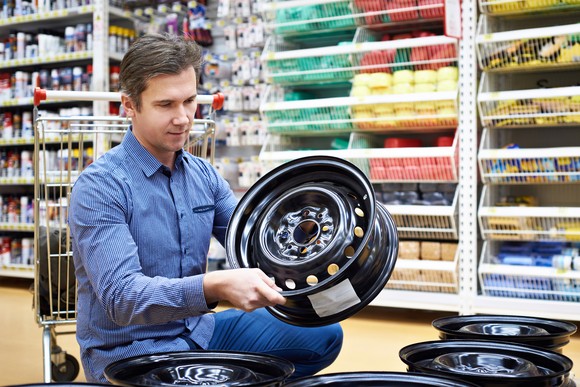 A customer in an auto parts store looks at wheel rims that are for sale there. In the background are shelves with other auto parts sitting on the shelves.