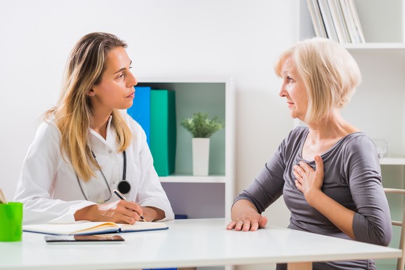 A physician sitting near a person with hand over heart.