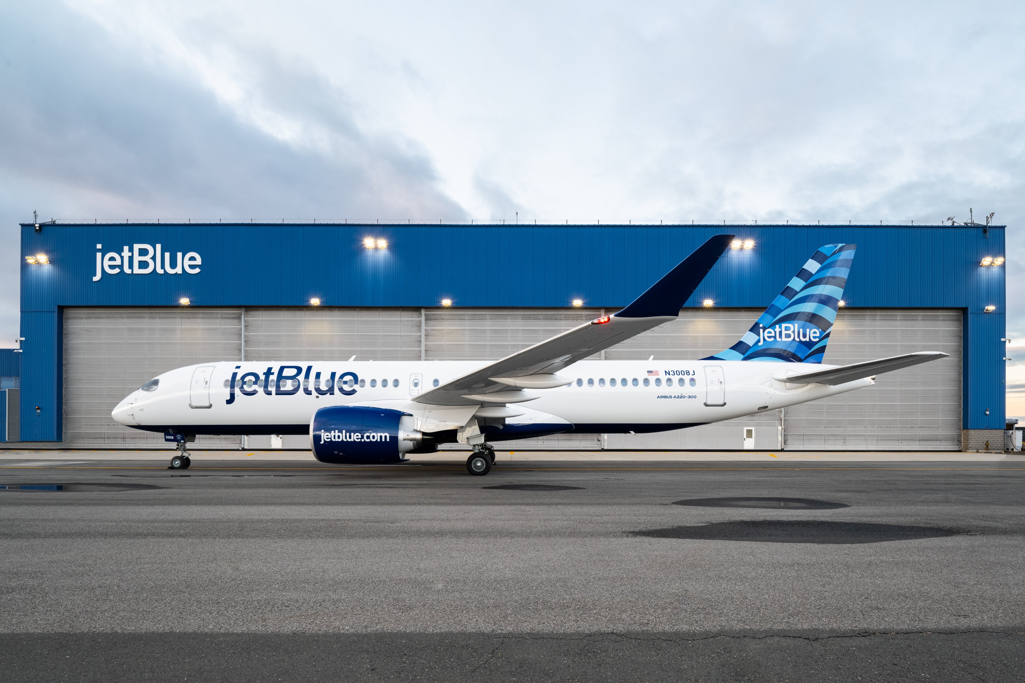 A JetBlue A220 parked in front of a hanger.