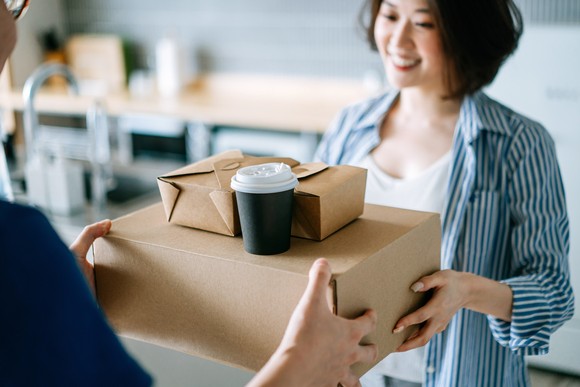 Two people hold a stack of several cardboard boxes.