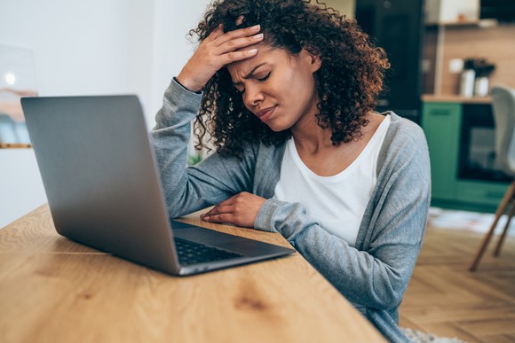 A person sits in front of a laptop with their head in their hands.