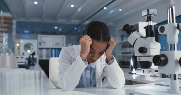 A lab scientist holding their head down.