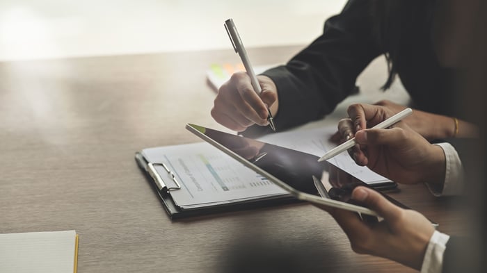 Two people using a tablet and paper documents.