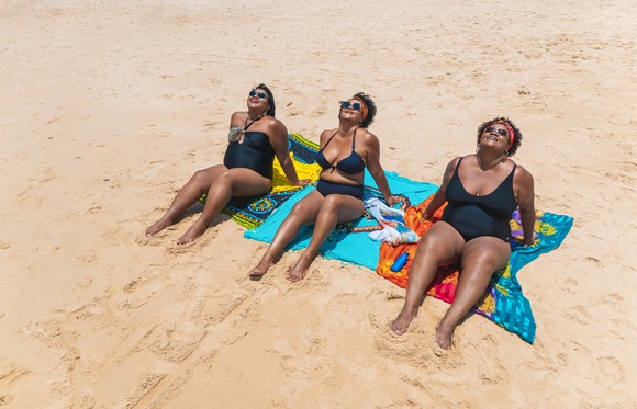 Three people on a beach lying on towels.
