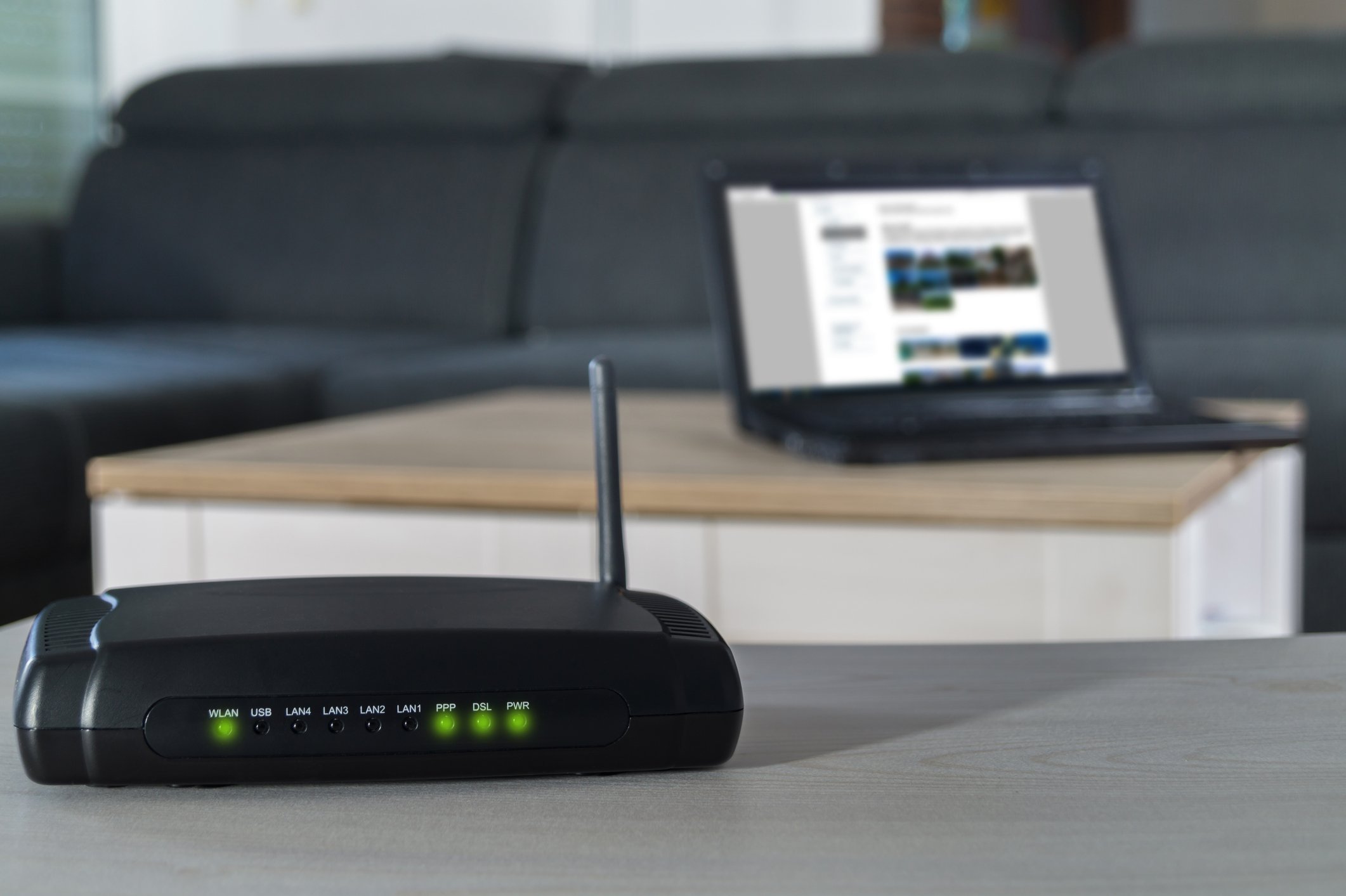 A wireless router on a living room table with laptop in the background. 