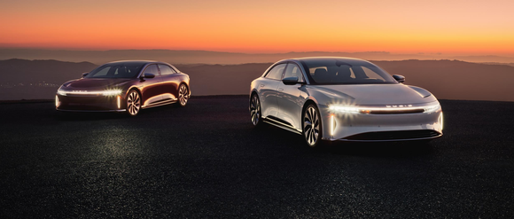Two Lucid Air electric sedans with lights on at sunset. 