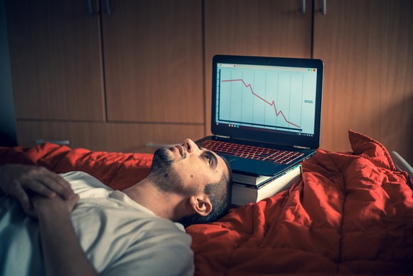 A person lies face up in front of laptop showing a market crash. 