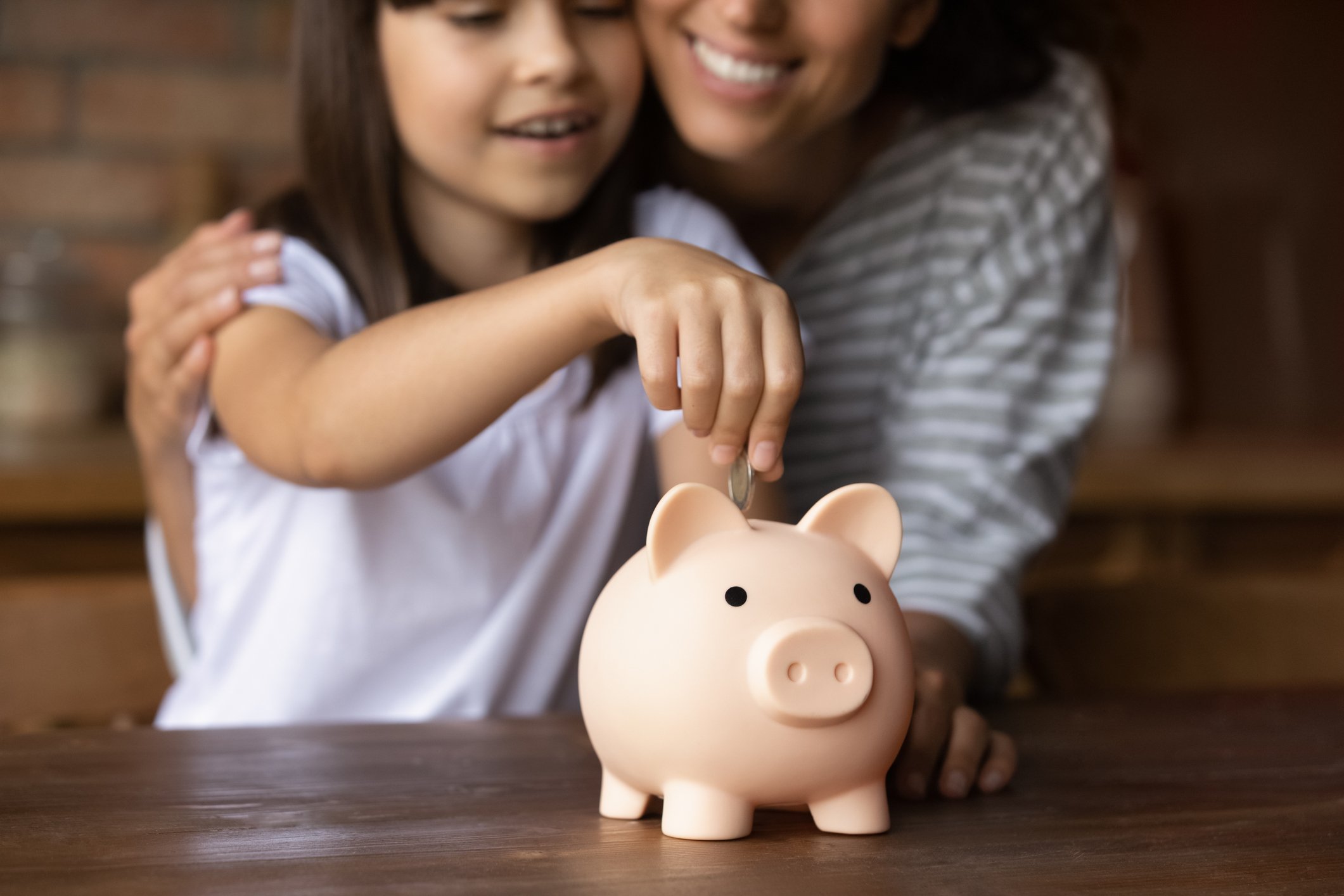 A parent and child add money to a piggy bank.