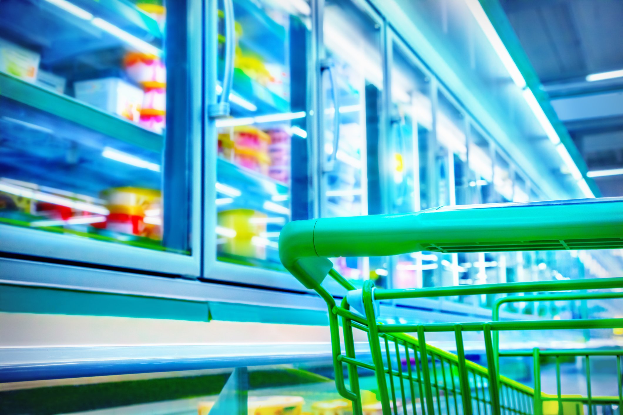 Green shopping cart in frozen food aisle in grocery store