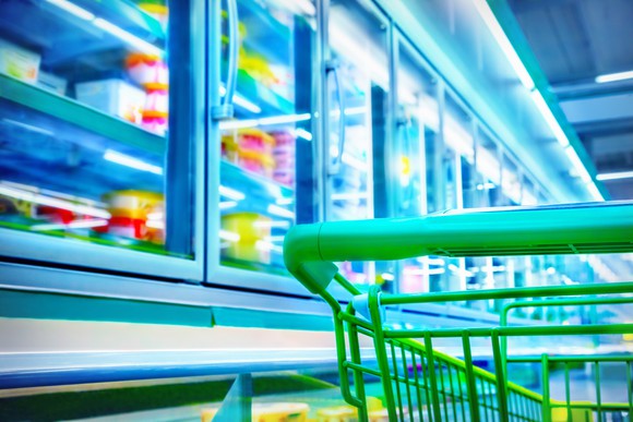 Green shopping cart in frozen food aisle in grocery store