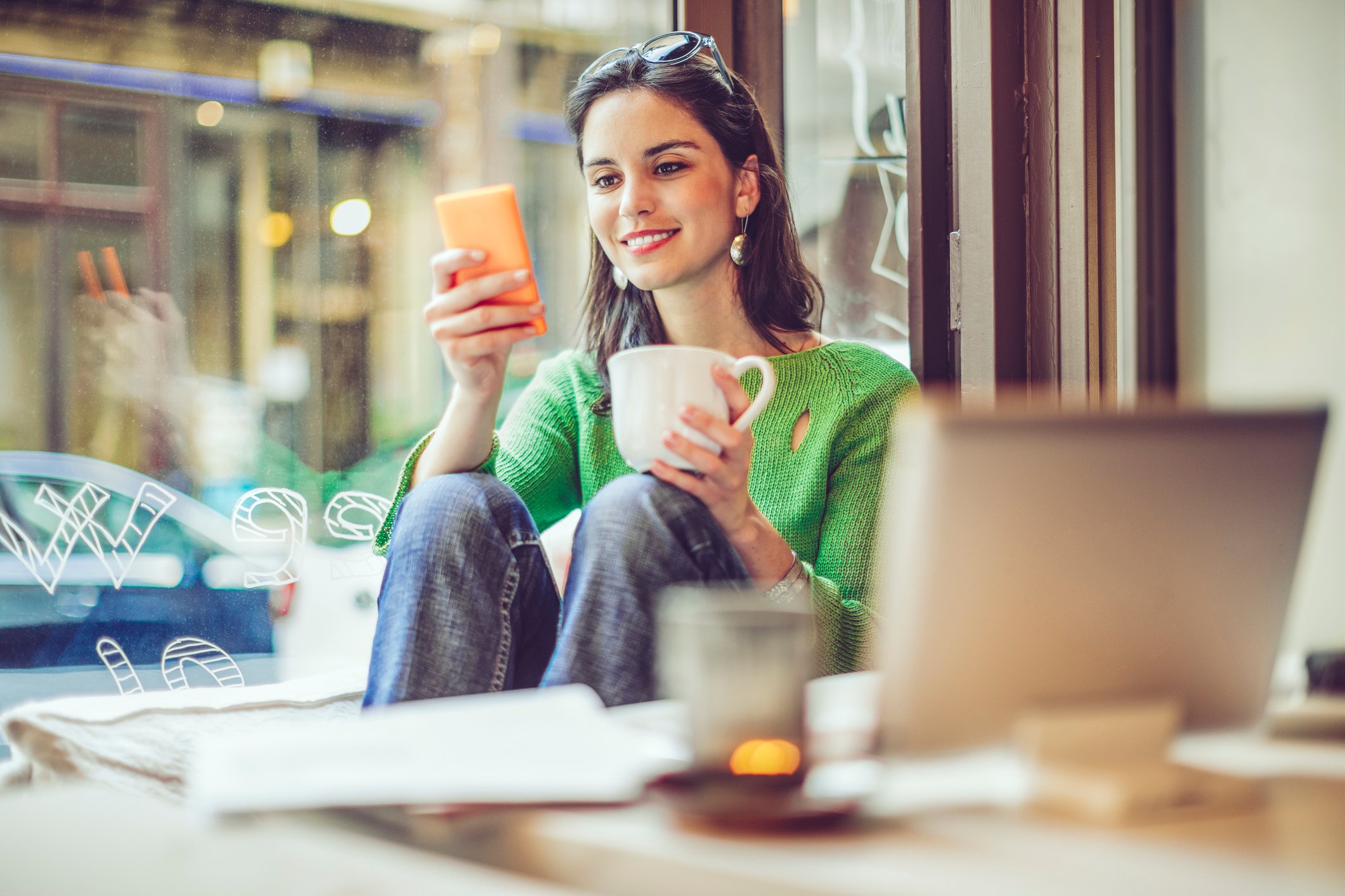 Person browsing on smartphone while sipping coffee.