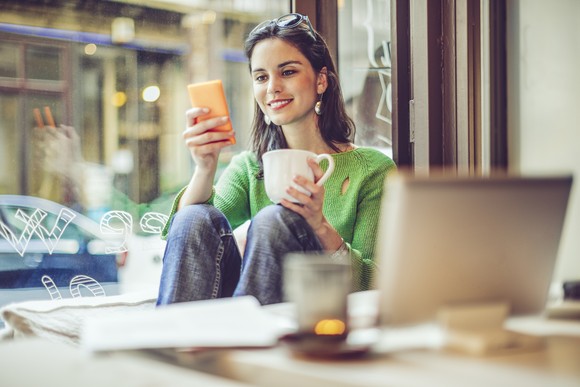Person browsing on smartphone while sipping coffee.