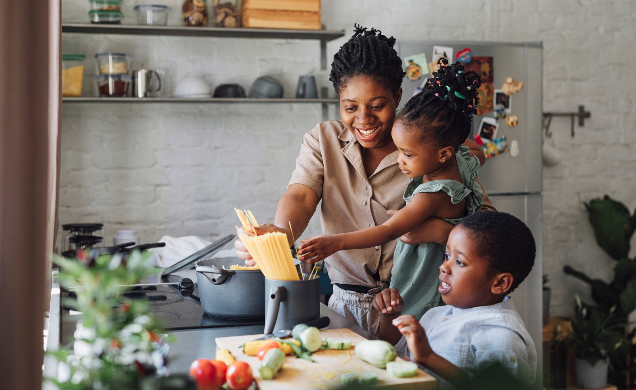 Adult person in a kitchen cooking a meal with two children.