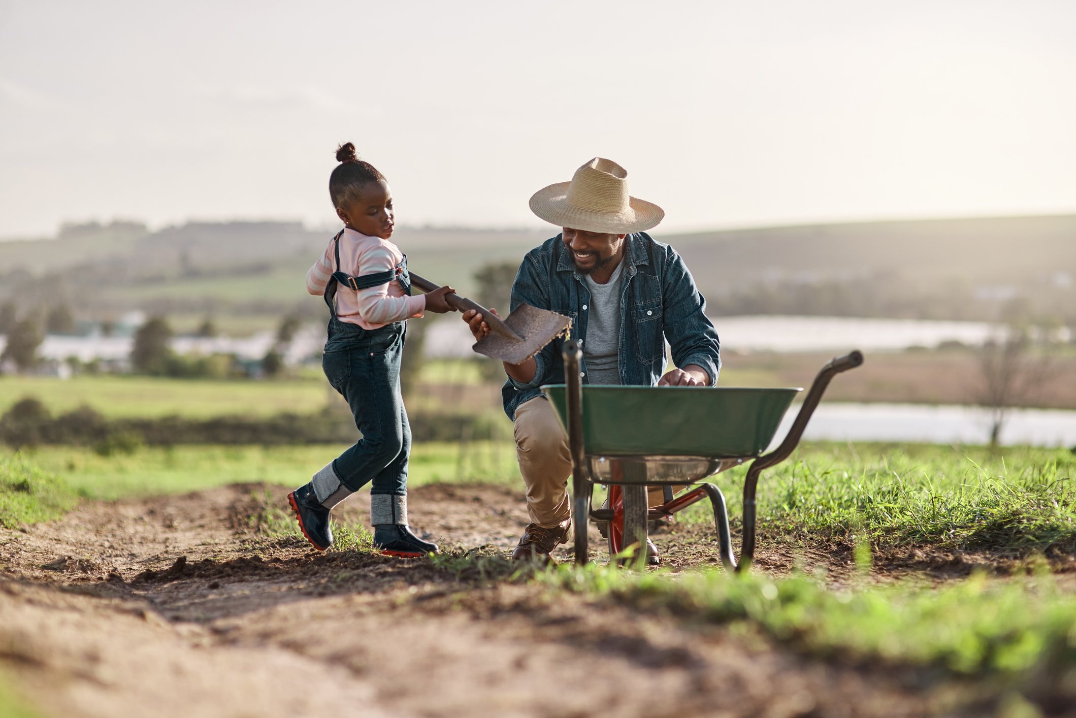 An adult and a child on a farm with a wheelbarrow.