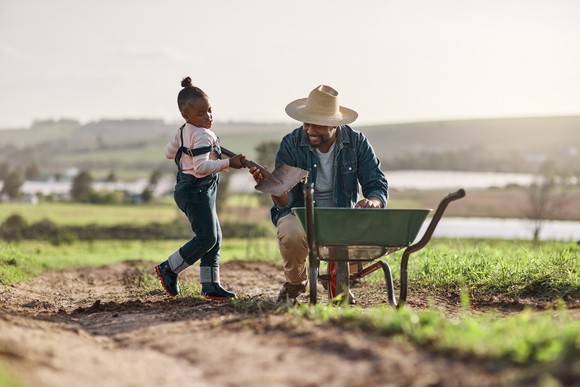 An adult and a child on a farm with a wheelbarrow.
