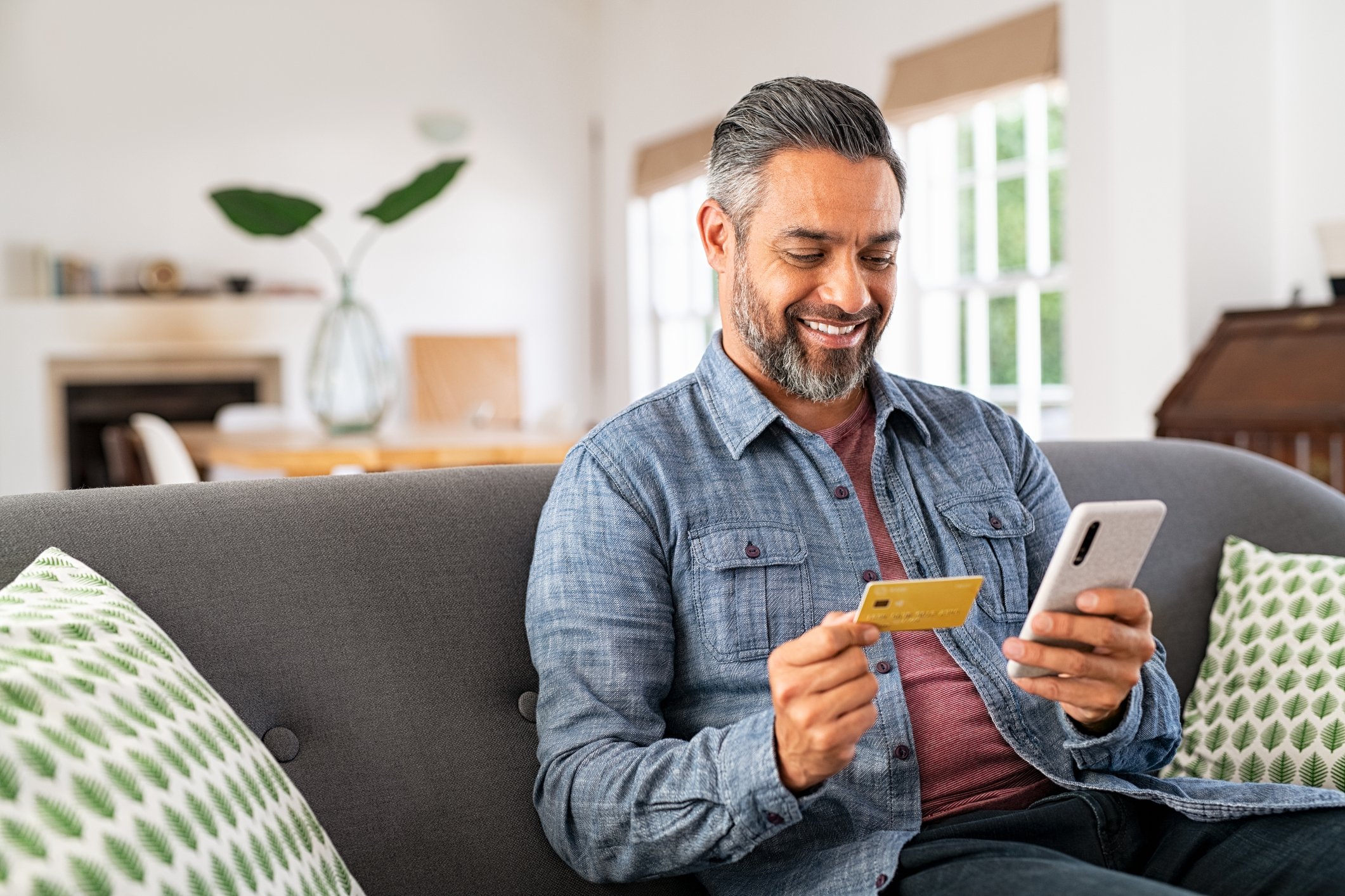 A person sits on a couch holding a smartphone and a credit card.