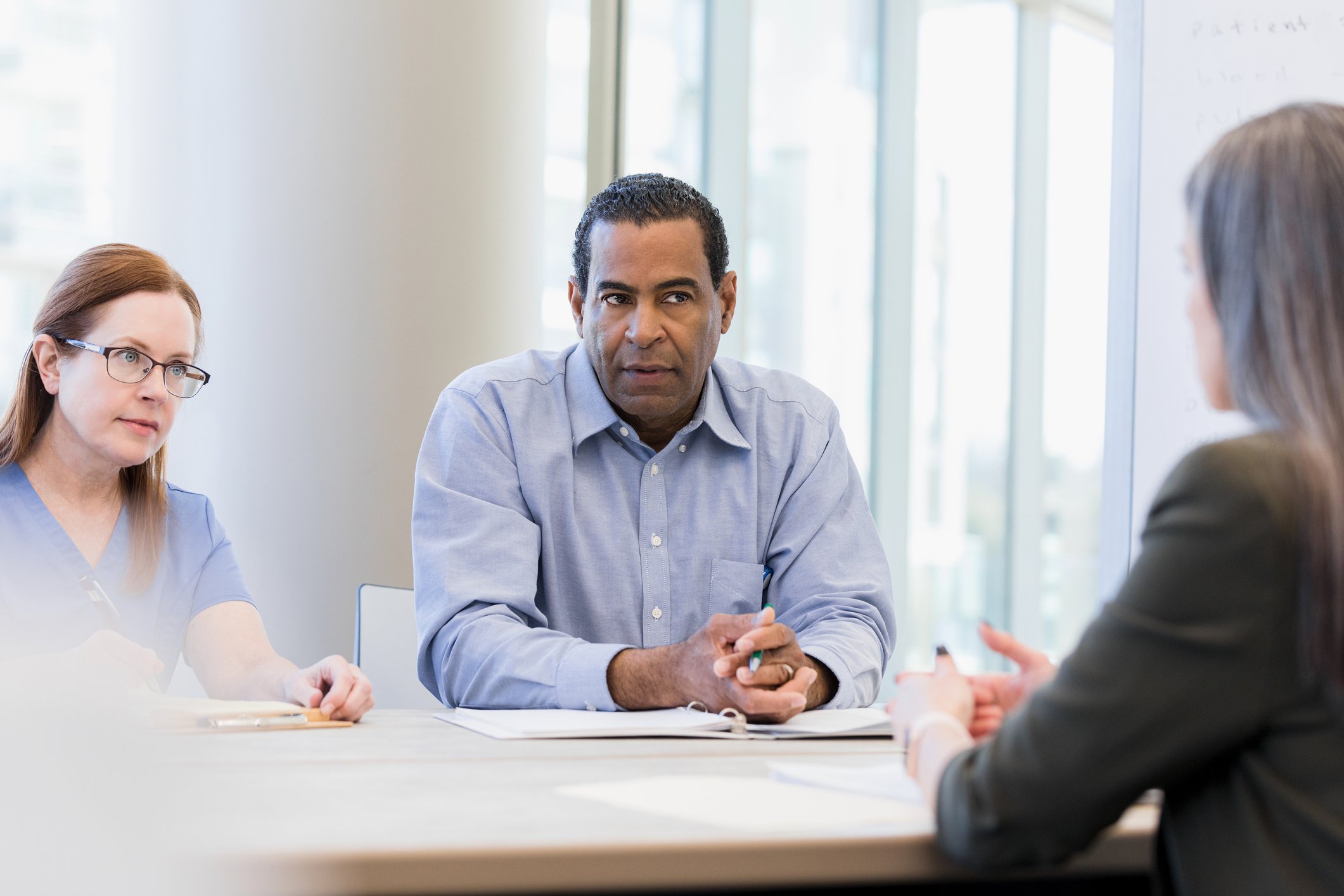 Two people sitting at a conference table listening to a third person speaking.