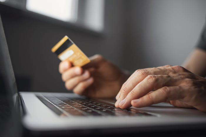 Person with credit card in front of laptop.