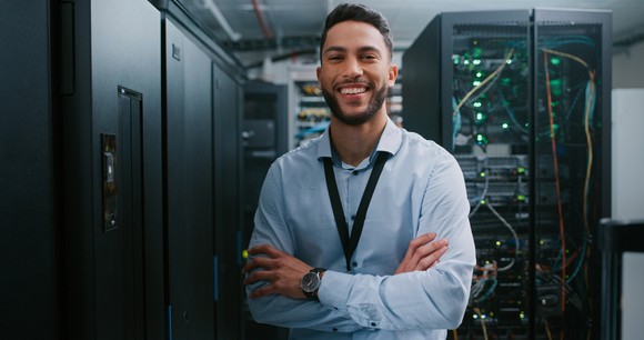 Person standing in front of a server stack and smiling.