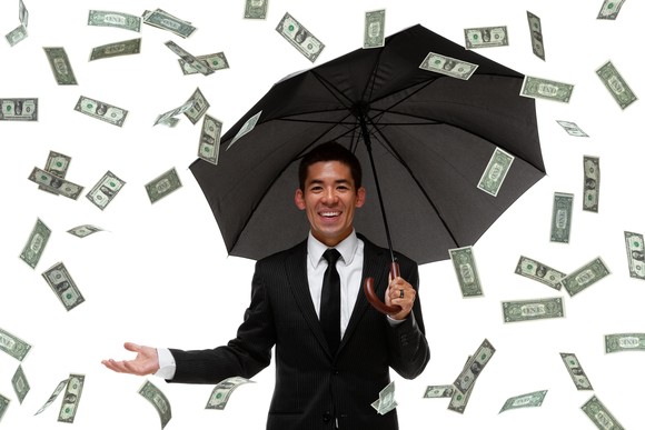 Businessman with an umbrella smiles as money rains down on him.