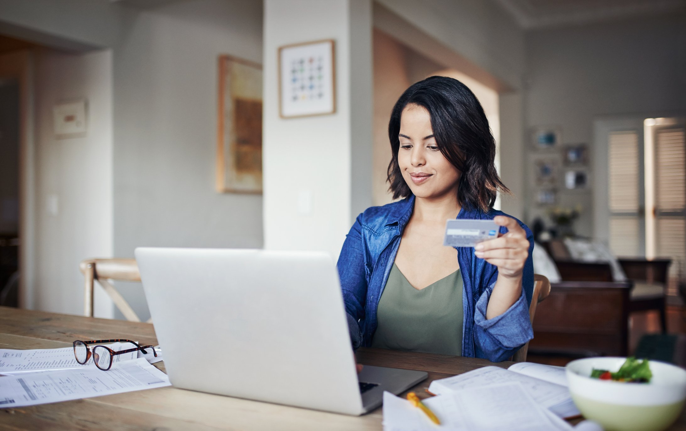 An online shopper uses a laptop at home while holding a credit card.