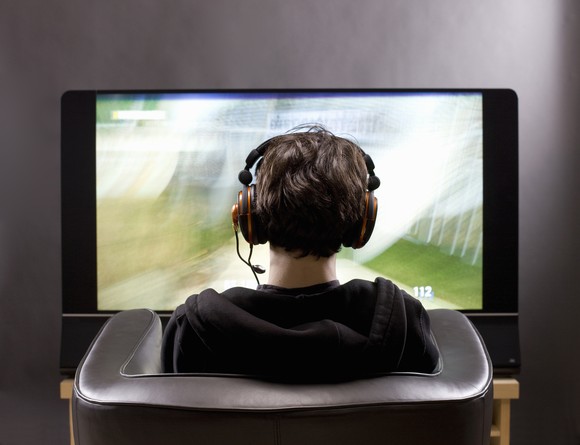 A person sitting in front of a screen and wearing a headset.