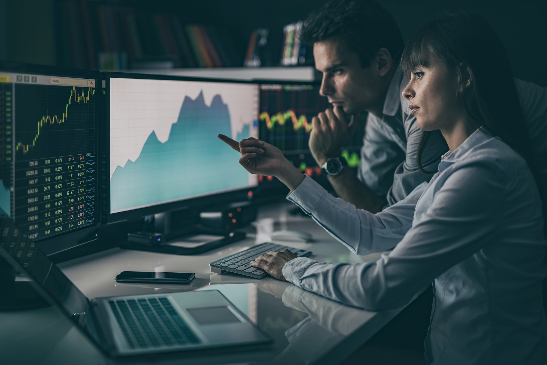 People are looking at a rising stock chart on computer screens. 