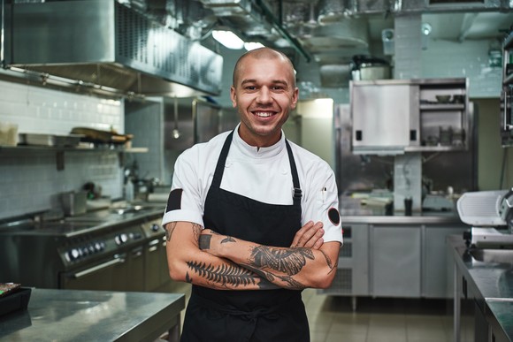 A kitchen worker is smiling, with crossed arms.