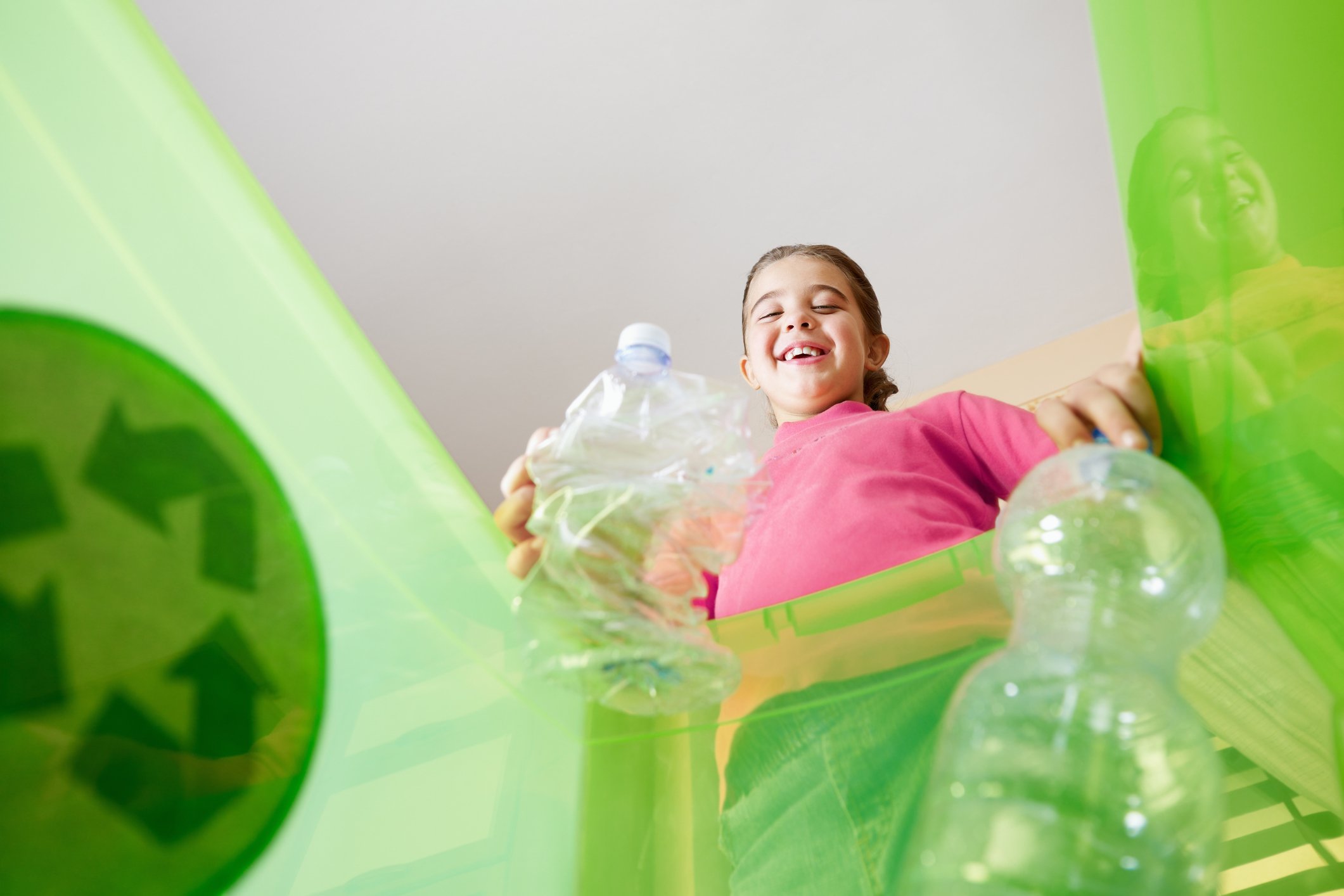 A girl smiles while tossing plastic bottles into a recycling bin. 