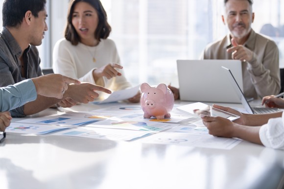 People sitting around a table pointing to a piggy bank.