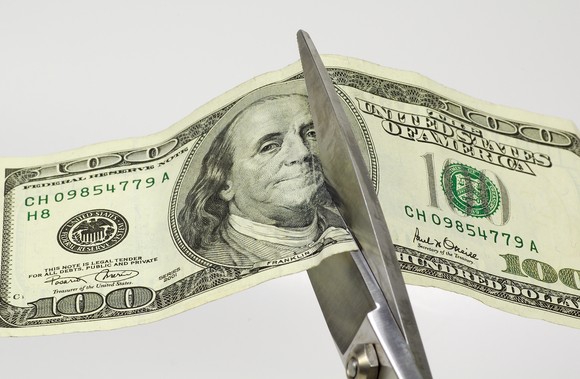 Scissors cutting through a one hundred dollar bill.  