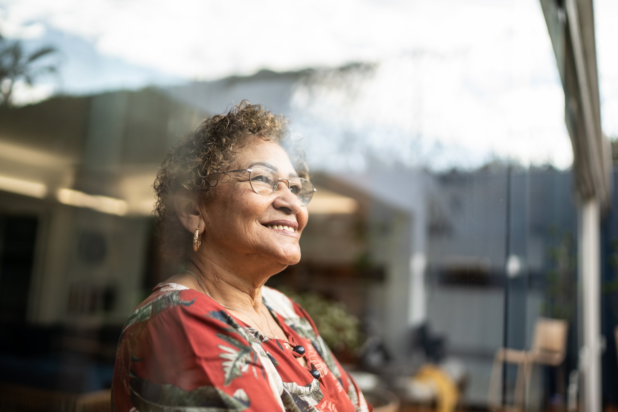 Older person looking out a window and smiling.